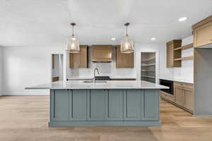 Kitchen featuring hanging light fixtures, light wood finished floors, a large island, light stone countertops, and a textured ceiling