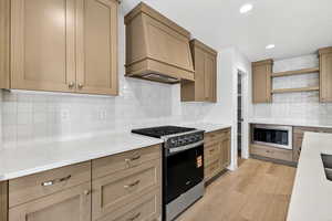 Kitchen with stainless steel appliances, open shelves, premium range hood, light stone counters, and recessed lighting