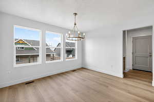 Unfurnished dining area featuring a chandelier, a textured ceiling, and light wood-style flooring