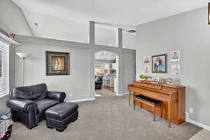 Living area featuring light colored carpet, arched walkways, and high vaulted ceiling