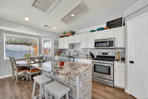 Kitchen with decorative backsplash, stainless steel appliances, white cabinets, a breakfast bar area, and recessed lighting