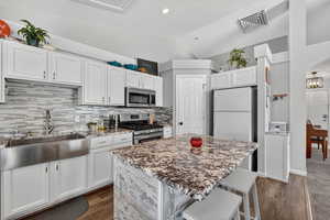 Kitchen with a breakfast bar area, stainless steel appliances, a kitchen island, white cabinetry, and lofted ceiling