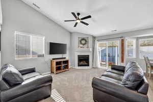 Living area featuring vaulted ceiling, a tile fireplace, healthy amount of natural light, carpet floors, and a ceiling fan