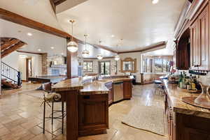 Kitchen with a breakfast bar area, a fireplace, stone tile flooring, dark brown cabinets, and decorative light fixtures