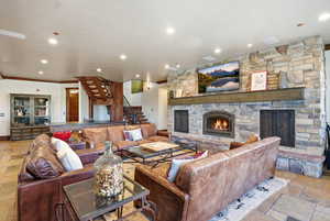 Living area featuring stone tile floors, a stone fireplace, recessed lighting, crown molding, and stairway