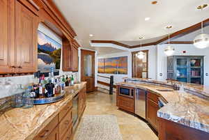 Kitchen with brown cabinetry, decorative light fixtures, stone tile floors, and recessed lighting