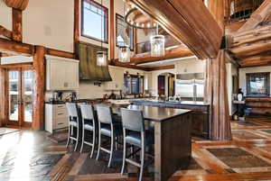 Kitchen with a kitchen bar, decorative light fixtures, an island with sink, dark brown cabinets, and custom exhaust hood
