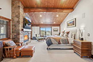 Carpeted bedroom featuring recessed lighting, a wooden ceiling with exposed beams, a stone fireplace, and high vaulted ceiling
