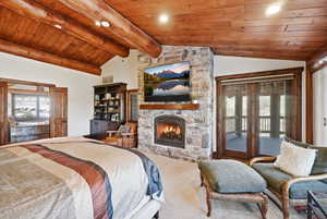 Bedroom featuring wooden ceiling, lofted ceiling, a stone fireplace, access to outside, and carpet
