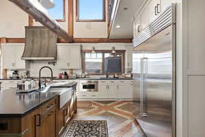 Kitchen with inlaid floor details, appliances with stainless steel finishes, brown cabinets, extractor fan, and white cabinets