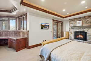 Bedroom featuring a tray ceiling, access to exterior, crown molding, light colored carpet, and a fireplace