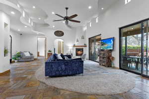 Living room featuring a glass covered fireplace, recessed lighting, stone tile floors, arched walkways, and a ceiling fan