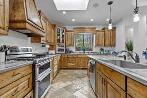 Kitchen featuring appliances with stainless steel finishes, brown cabinetry, pendant lighting, recessed lighting, and custom range hood