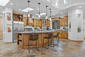 Kitchen with a skylight, open shelves, stone tile flooring, stainless steel appliances, and brown cabinetry
