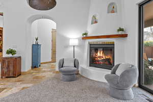 Sitting room with stone tile floors, arched walkways, a glass covered fireplace, and carpet