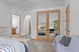 Primary Suite. Carpeted bedroom with french doors, connected bathroom, and arched walkways