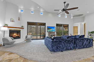 Living room featuring a glass covered fireplace, stone finish floors, ceiling fan, a high ceiling, and recessed lighting