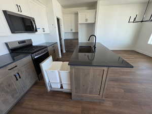 Dual tone kitchen with stainless steel appliances, an island with sink, dark wood-style floors, two tone cabinets, and decorative backsplash