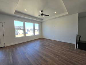 Unfurnished living room featuring a ceiling fan, a raised ceiling, dark wood finished floors, and recessed lighting