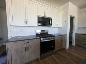 Kitchen featuring stainless steel appliances, two tone cabinets, decorative backsplash, dark wood-type flooring, and dark stone counters