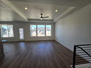 Unfurnished living room featuring a tray ceiling, ceiling fan, recessed lighting, and dark wood-style flooring