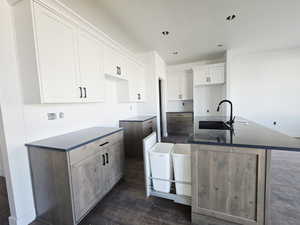 Kitchen featuring white cabinets, a center island with sink, and dark wood-style floors