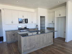 Dual tone kitchen with dual tone cabinetry, stainless steel appliances, an island with sink, dark wood-type flooring, and backsplash