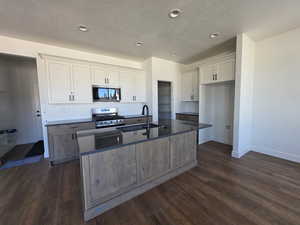 Two tone kitchen with a center island with sink, dark wood-style floors, stainless steel appliances, two tone cabinets, and decorative backsplash