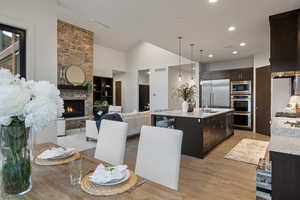 Kitchen with light stone countertops, a large fireplace, built in appliances, pendant lighting, and an island with sink