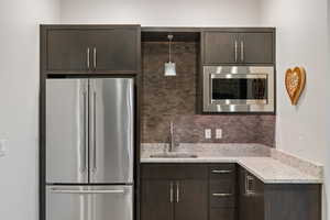 Kitchen featuring dark brown cabinetry, stainless steel appliances, light stone countertops, tasteful backsplash, and decorative light fixtures