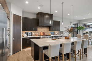 Kitchen with light stone countertops, hanging light fixtures, a kitchen breakfast bar, recessed lighting, and light wood-style floors