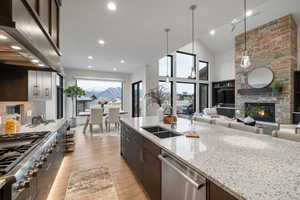 Kitchen with light stone countertops, stainless steel appliances, exhaust hood, hanging light fixtures, and high vaulted ceiling