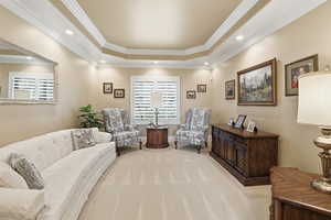 Sitting room with a raised ceiling, ornamental molding, light carpet, and recessed lighting