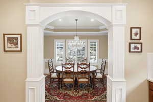 Dining room with decorative columns, a raised ceiling, ornamental molding, arched walkways, and a chandelier