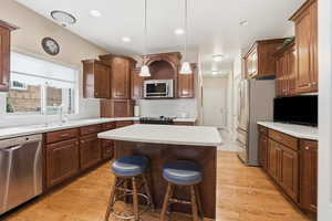 Kitchen featuring appliances with stainless steel finishes, decorative light fixtures, a center island, light countertops, and recessed lighting