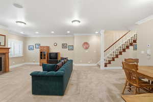 Living room with crown molding, light colored carpet, a tiled fireplace, and stairway