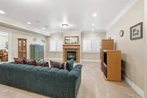 Living room with a glass covered fireplace, ornamental molding, light carpet, and recessed lighting