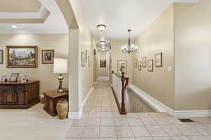Corridor with crown molding, light tile patterned floors, arched walkways, and a chandelier