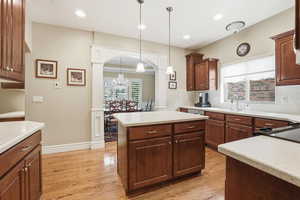 Kitchen with decorative light fixtures, light wood-style flooring, arched walkways, a center island, and a chandelier