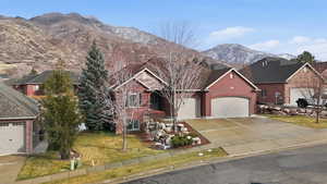 View of front facade featuring a mountain view, a front yard, driveway, brick siding, and an attached garage