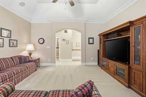 Living area featuring ornamental molding, light carpet, arched walkways, a ceiling fan, and vaulted ceiling