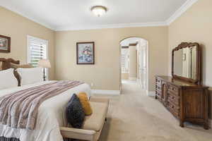Bedroom with arched walkways, crown molding, carpet floors, and connected bathroom