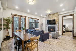 Dining room with light wood-type flooring, french doors, and a stone fireplace