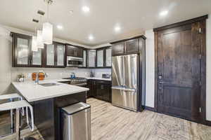 Kitchen with premium appliances, glass insert cabinets, hanging light fixtures, a peninsula, and a kitchen bar