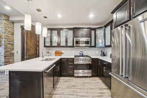 Kitchen featuring high quality appliances, a peninsula, decorative light fixtures, dark brown cabinetry, and glass insert cabinets