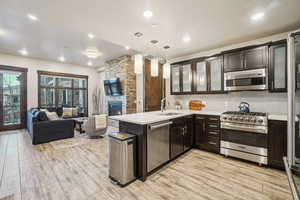 Kitchen with hanging light fixtures, high end appliances, glass insert cabinets, open floor plan, and light wood-type flooring