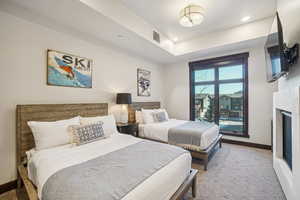 Bedroom featuring a fireplace, a raised ceiling, recessed lighting, and light carpet