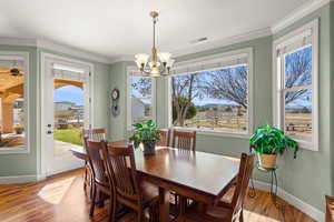 Dining space with wood finished floors, a chandelier, and ornamental molding