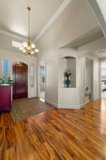 Entryway with arched walkways, wood finished floors, crown molding, a chandelier, and healthy amount of natural light