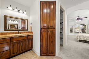 Ensuite bathroom featuring vanity, light carpet, a ceiling fan, a spacious closet, and light tile patterned floors